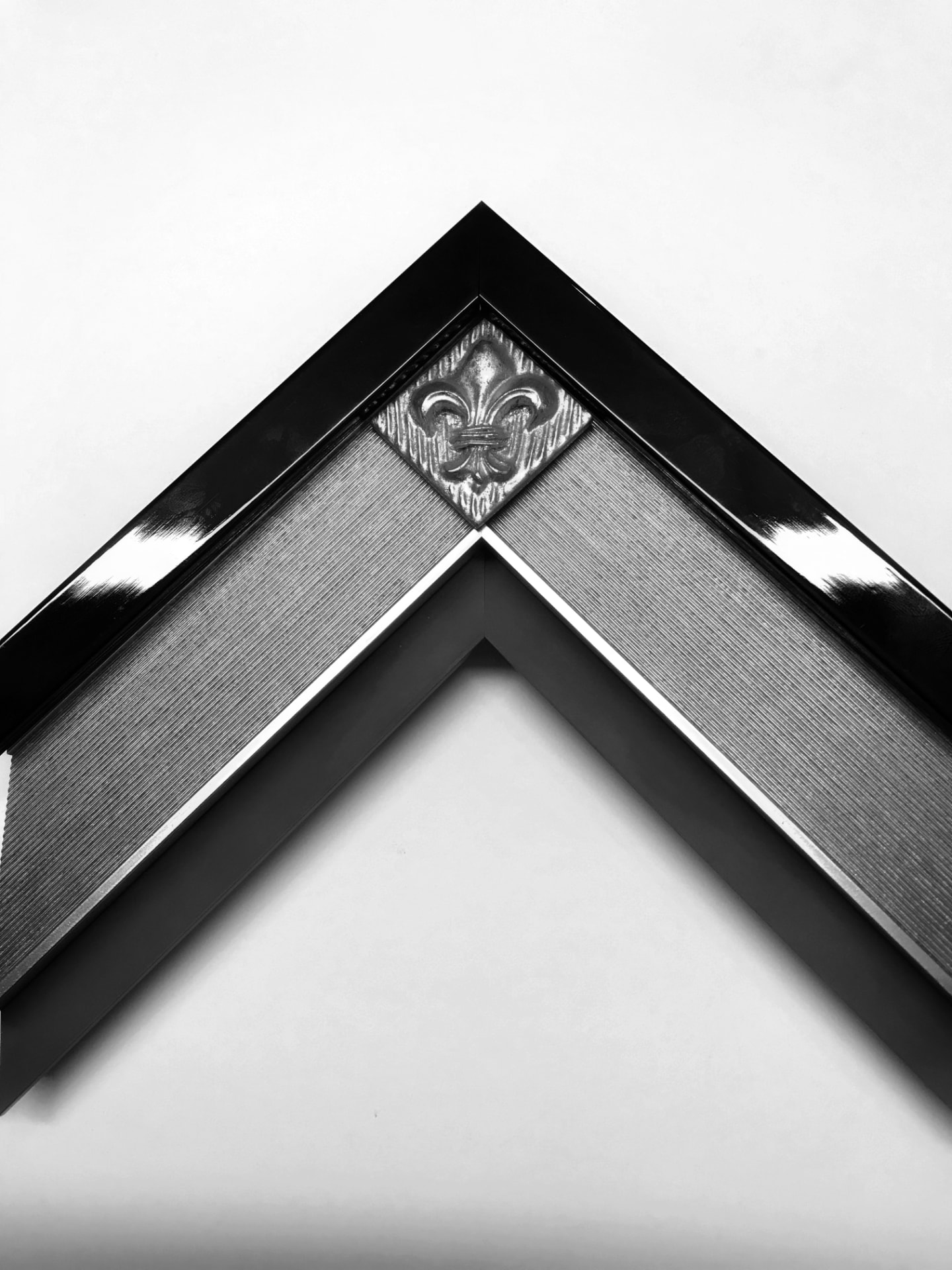 Corner of a glossy black frame with a textured silver liner and an ornate fleur-de-lis corner block