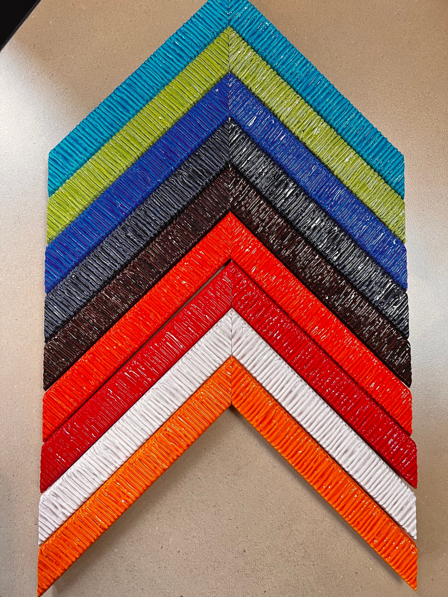 Stacked corner samples of glossy textured frame mouldings in turquoise, lime, blue, black, brown, orange, red, and white