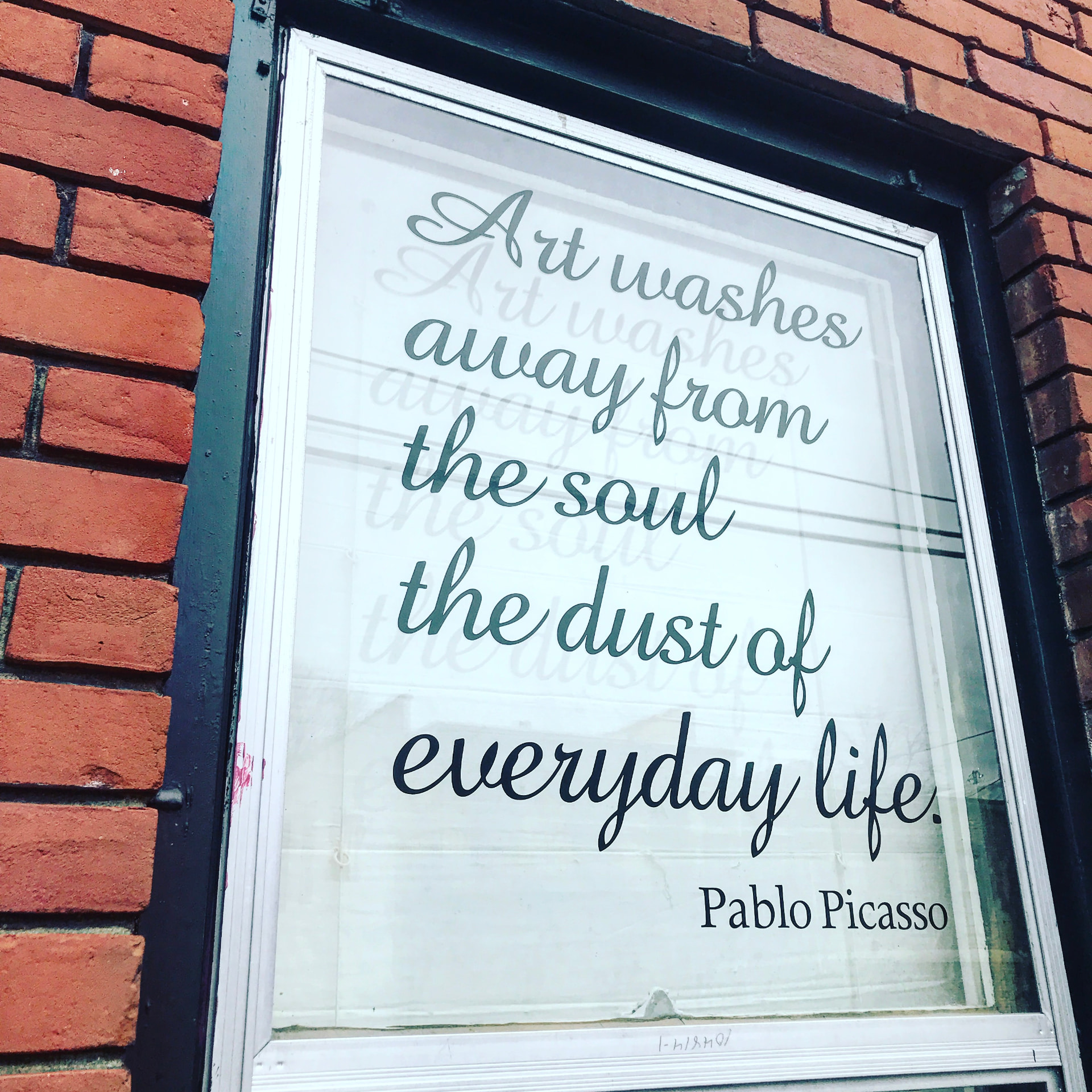 Shop window on a brick wall with the Pablo Picasso quote 'Art washes away from the soul the dust of everyday life' in script lettering